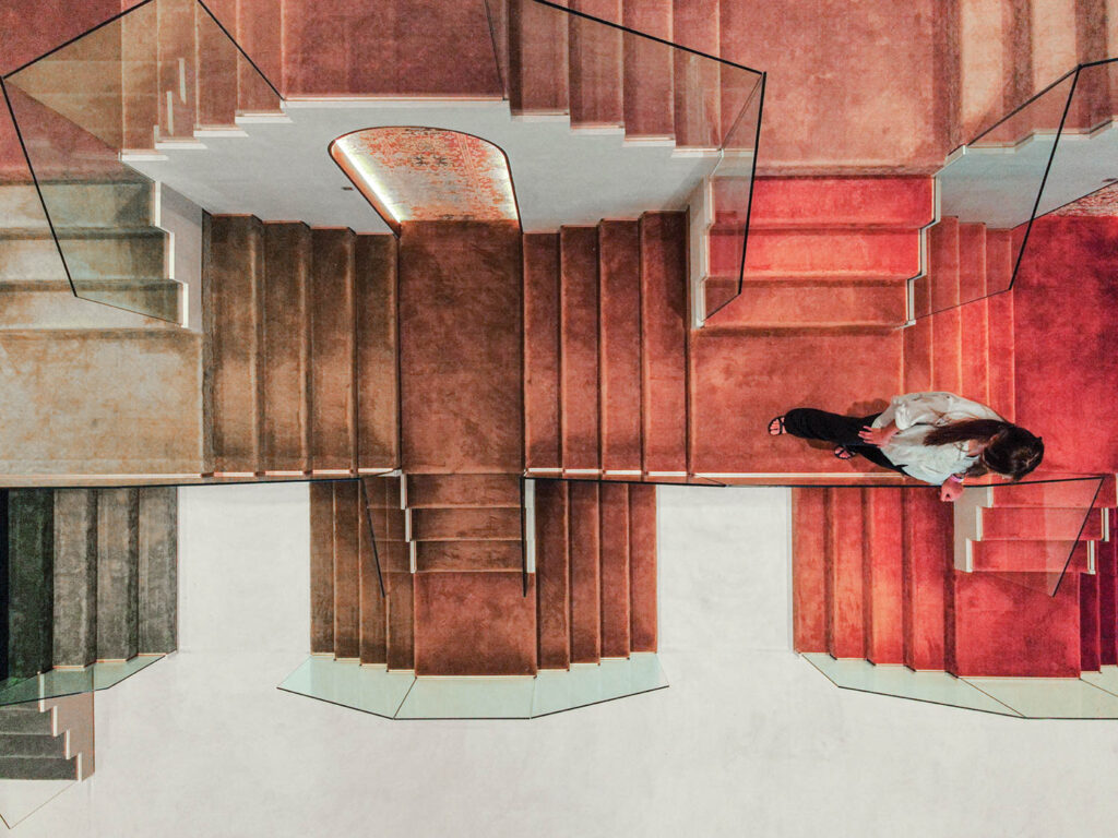 a woman walks down a staircase coated in Jaipur Rugs in red and brown tones