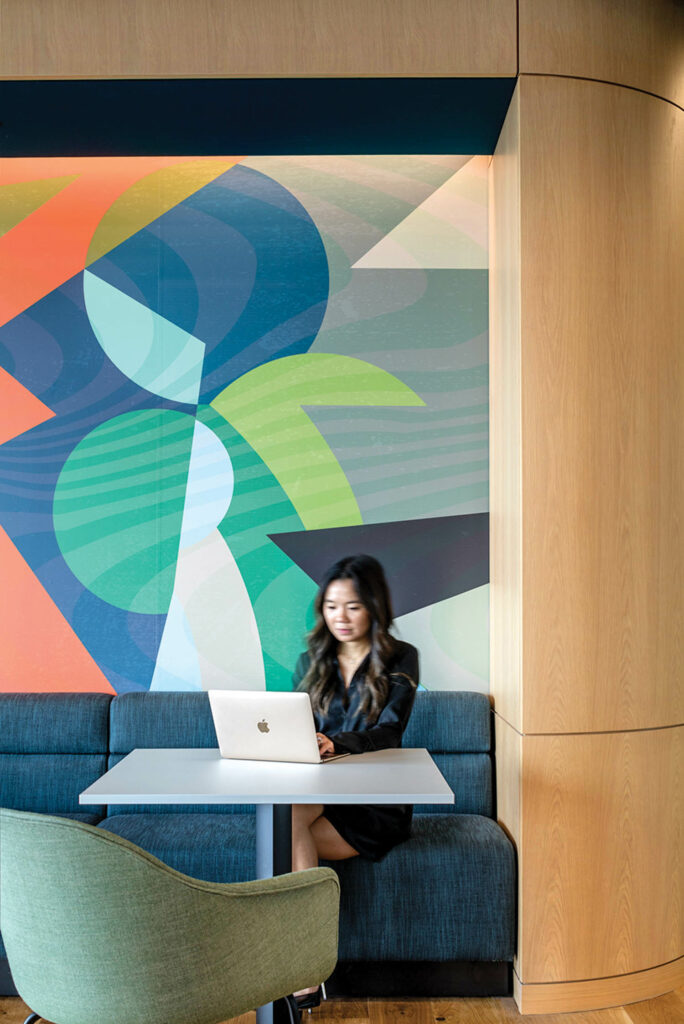 a woman works on a laptop in front of a colorful mural