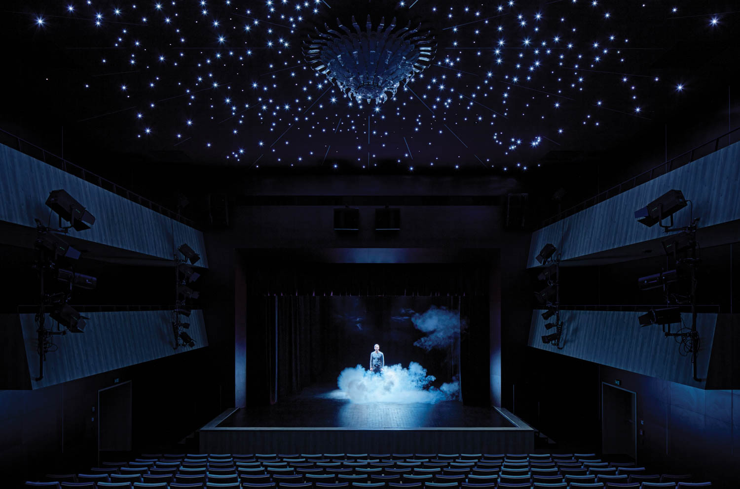 actor standing on a darkly-lit stage with smoke coming out