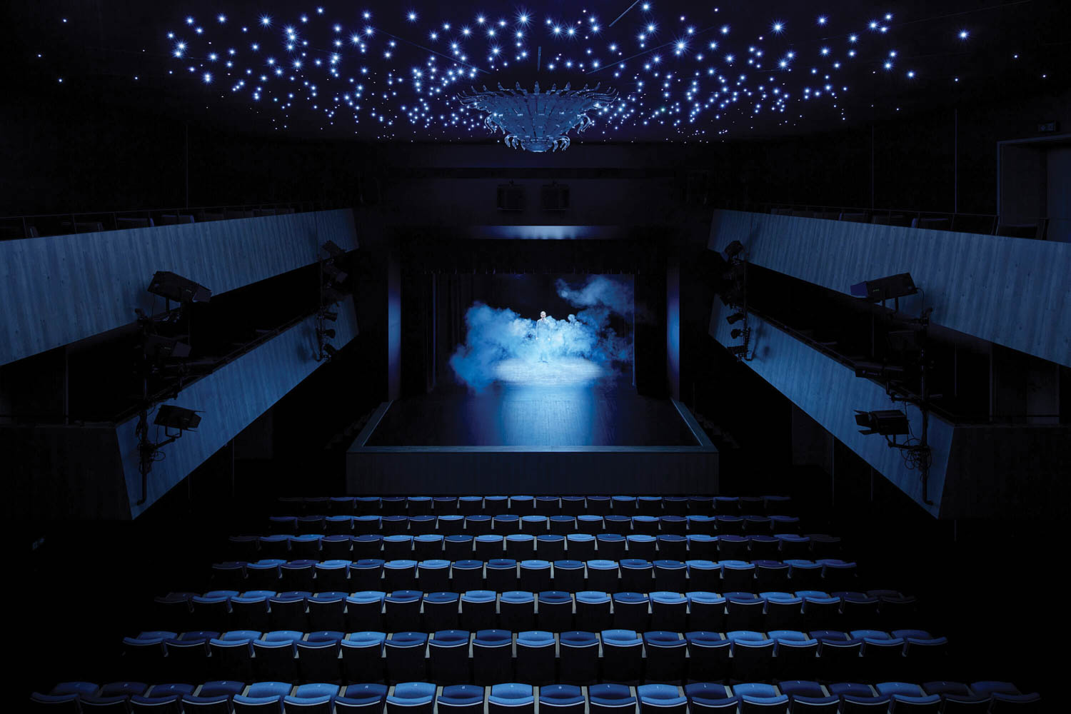 aerial view of a darkly-lit stage with blue seats on lights on ceiling