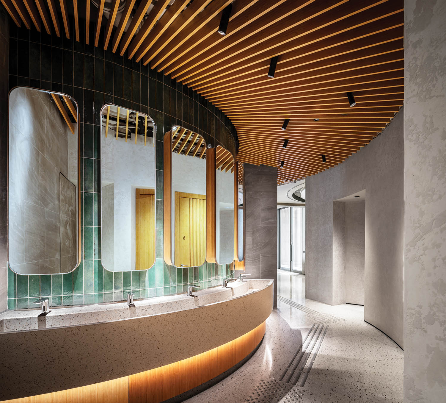 the restroom curves around with green tiles above the sinks