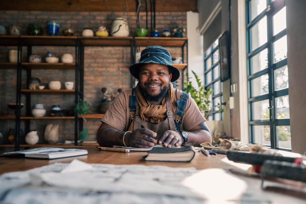 Andile Dyalvane sitting in his studio with his pieces behind him