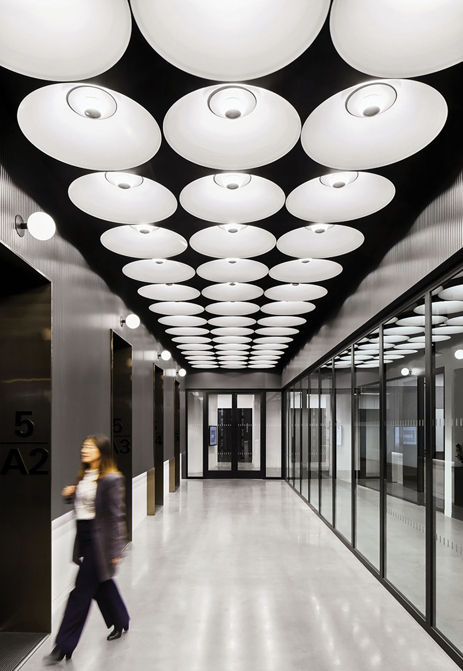 A woman walking down a long hallway with many lights.