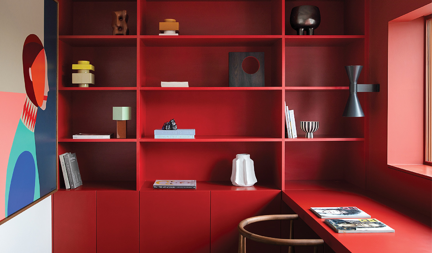 A red desk with a chair and a book shelf.