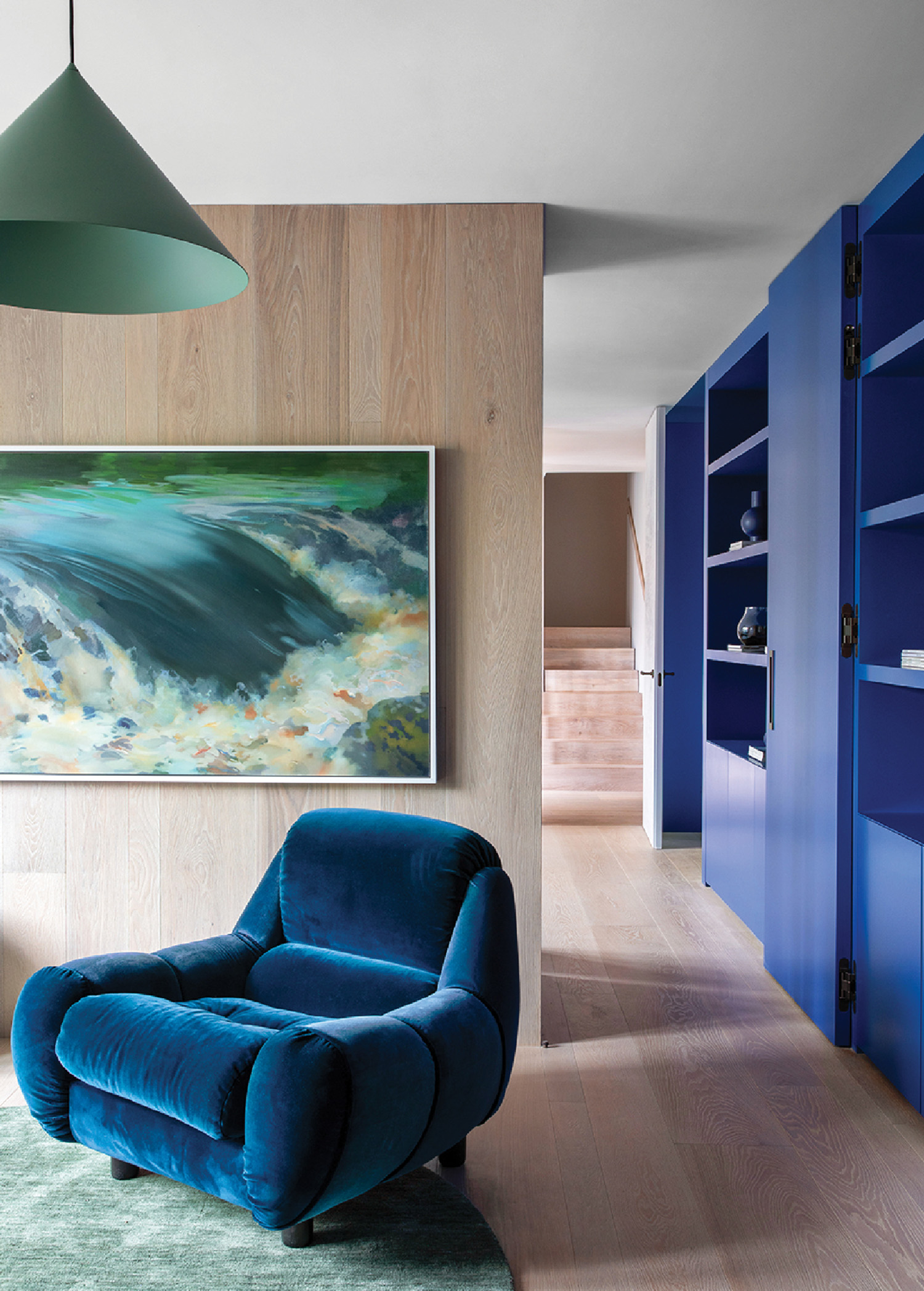 A blue chair in a living room with a painting on the wall