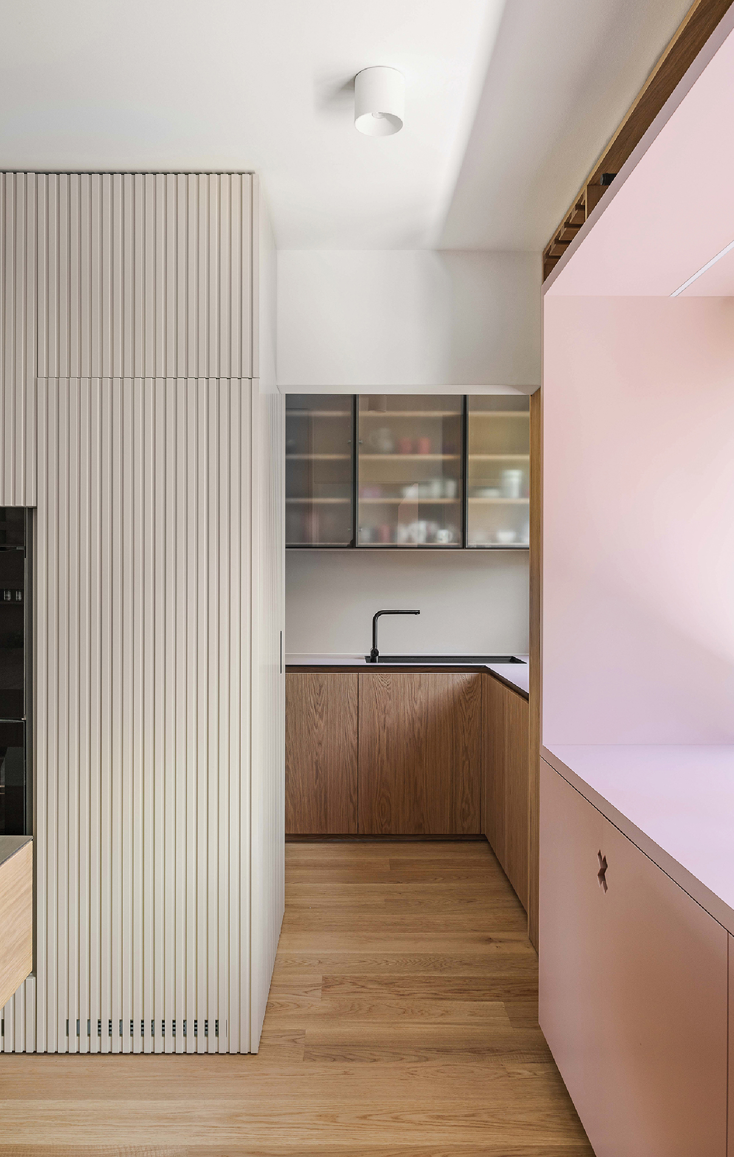 A kitchen with a pink wall and wooden floor.