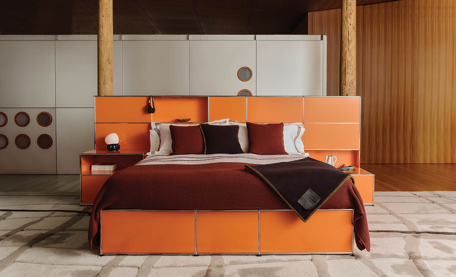 A bed with a red blanket and a white headboard.