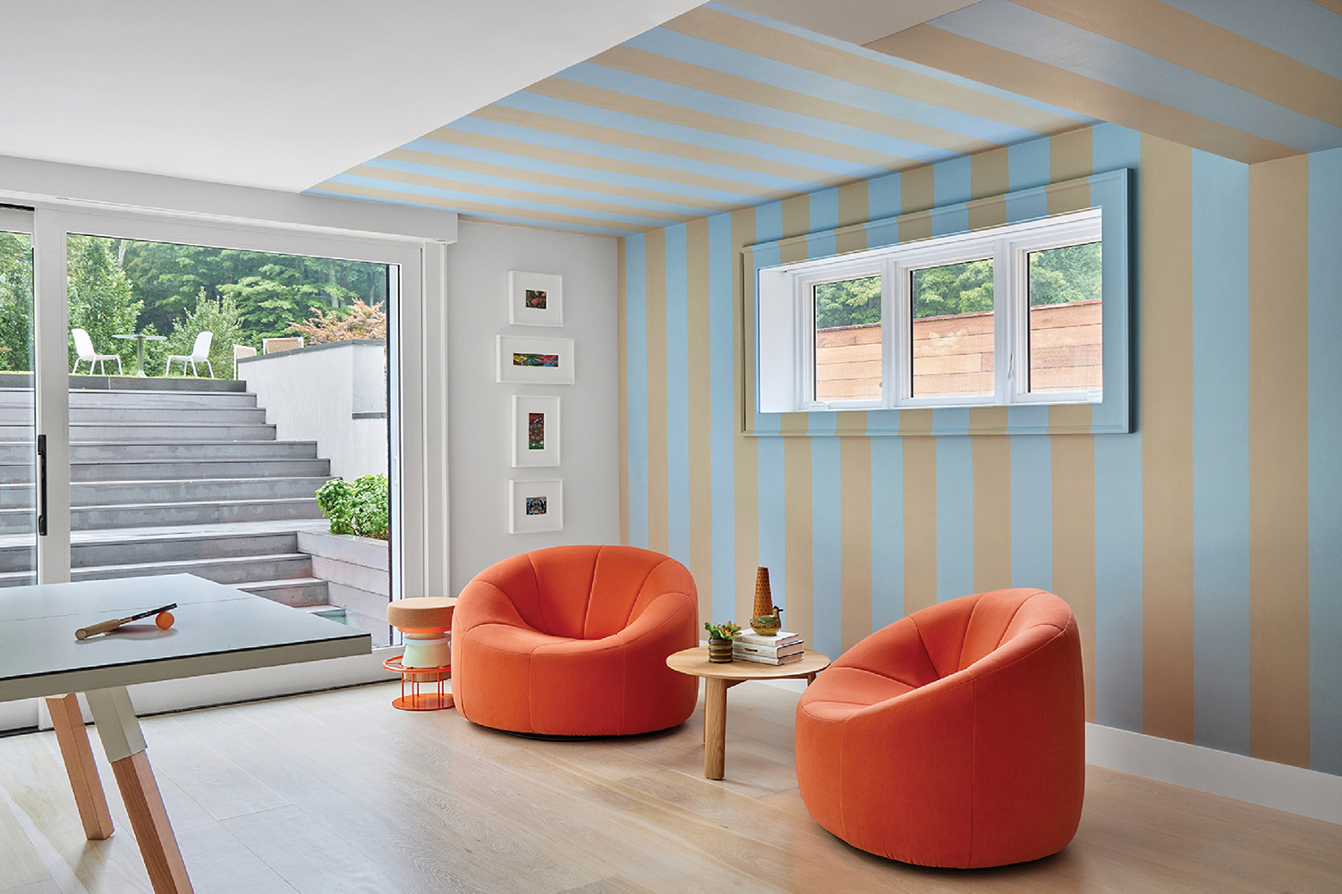 A living room with a striped wallpaper and orange chairs.