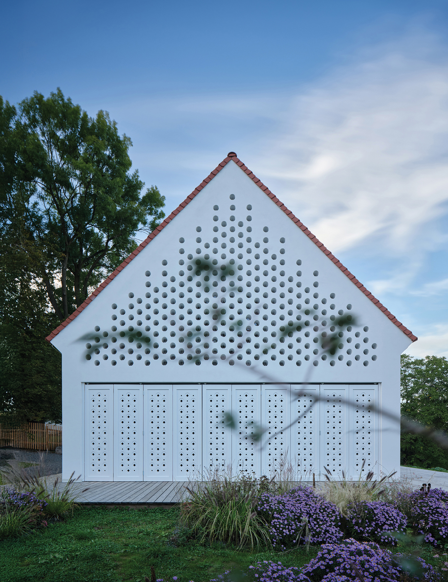 A white building with a red roof and a lot of purple flowers.