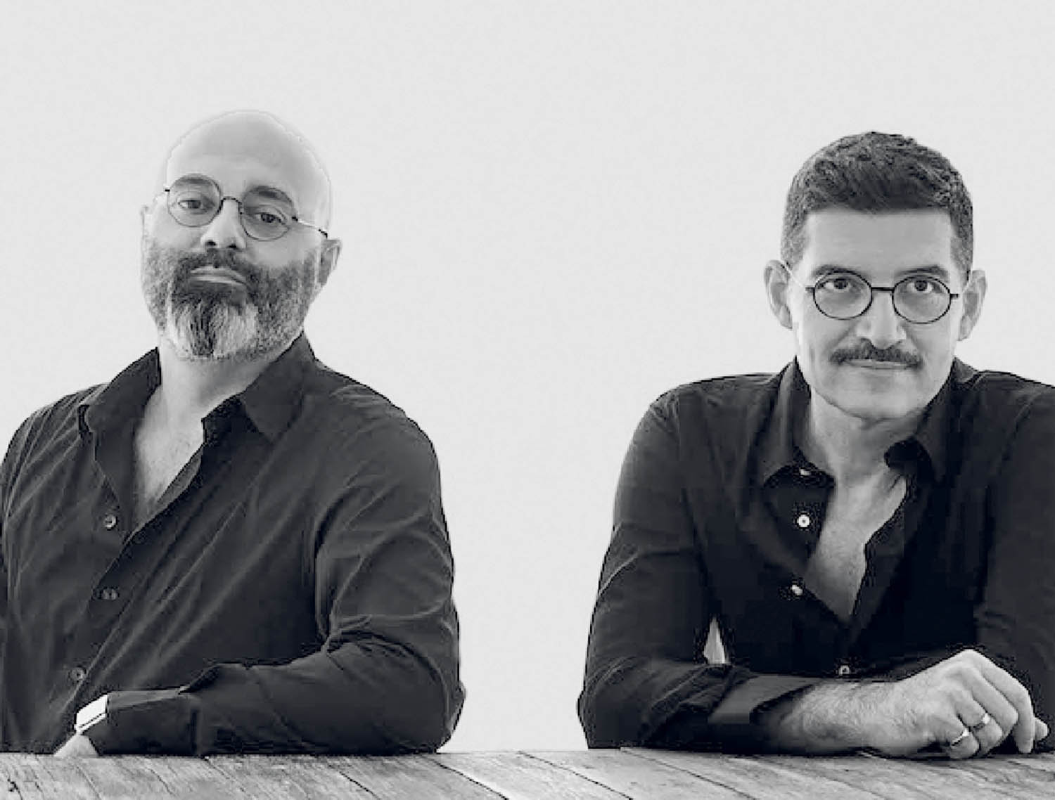 Two men sitting at a table with their arms crossed.