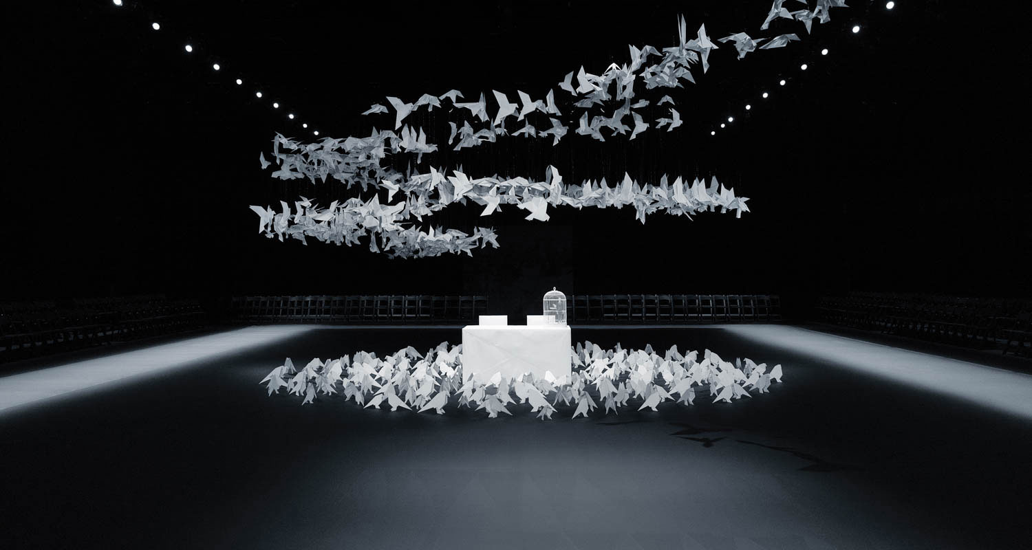 black fashion runway with a floating spiral of white birds above a white cube display