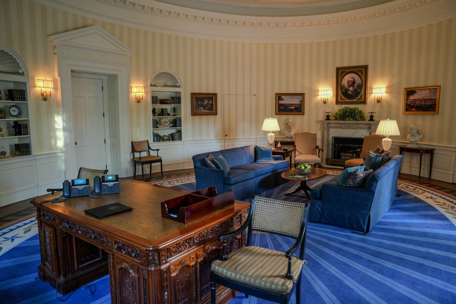 sitting area of White House with dark blue couches, wooden desk and artwork on wall