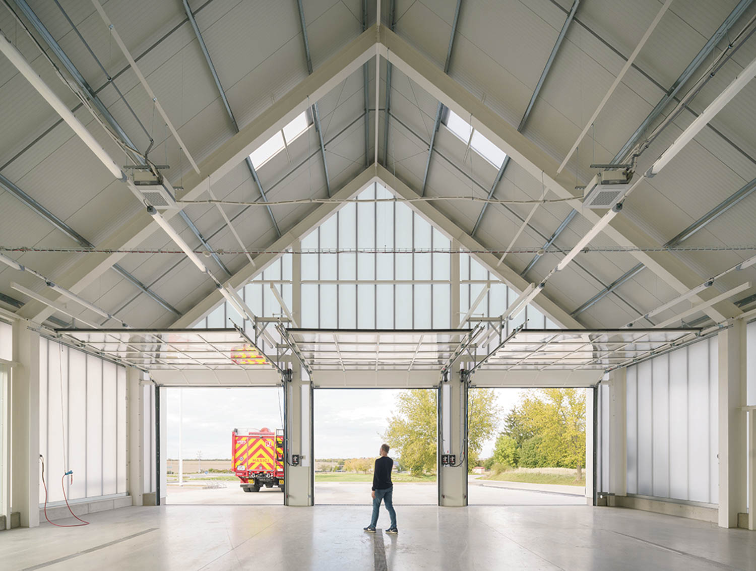 A man walking in a large warehouse with a fire truck in the back.