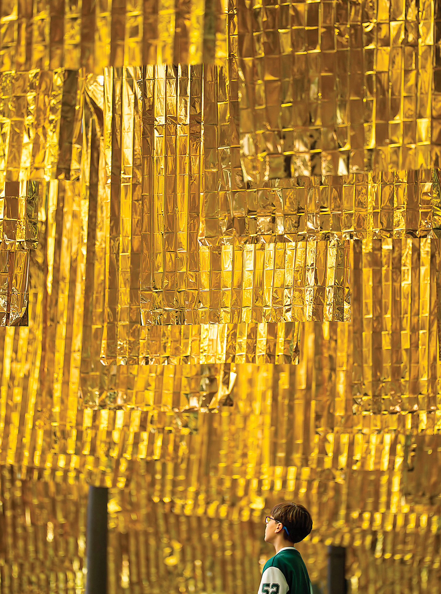A man sitting on a bench in front of a wall of gold foil.