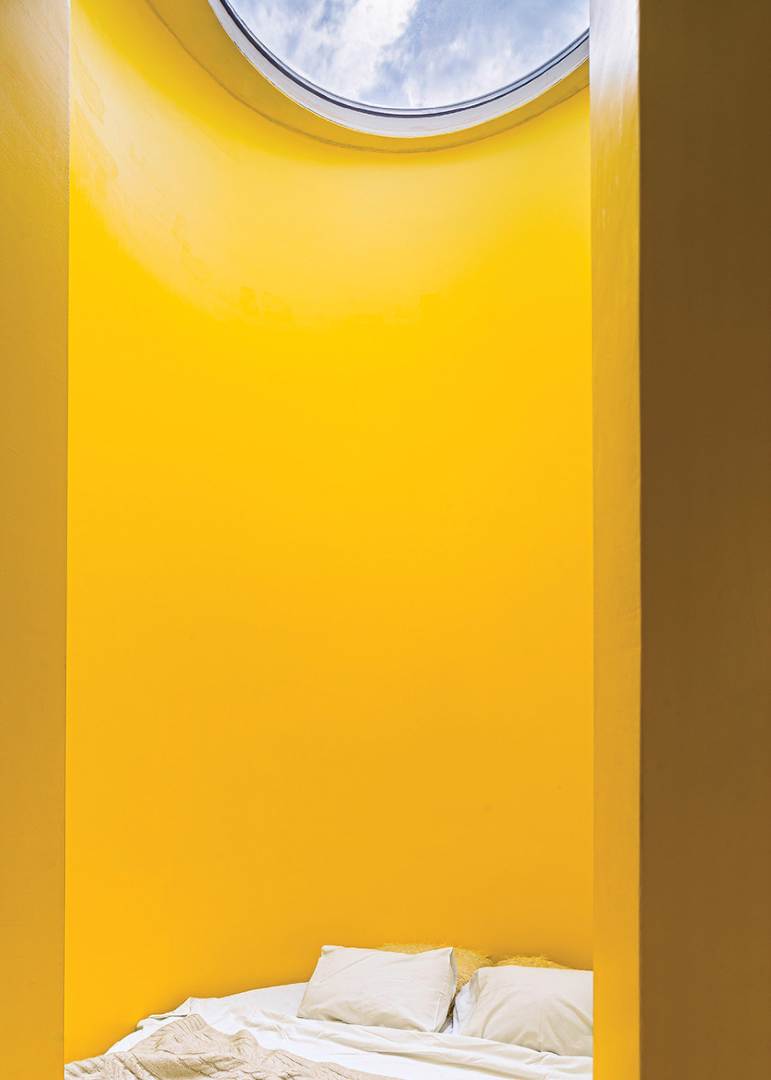 A bed in a yellow room with a skylight.