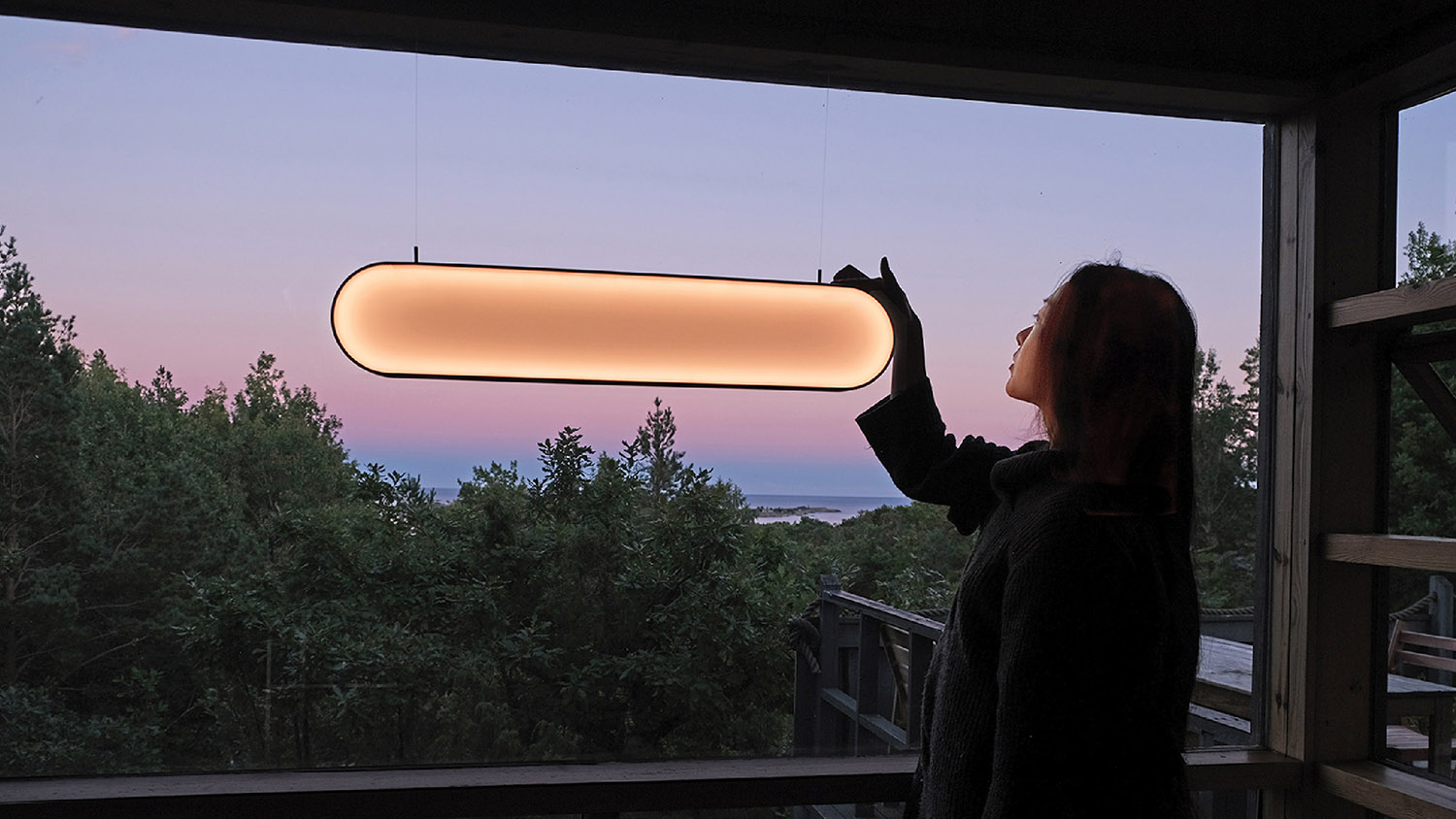 A woman is looking out a window at the sunset.