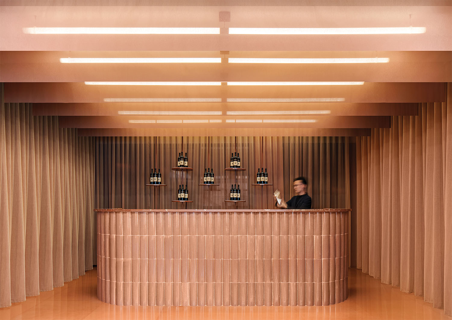 A woman standing behind a bar with bottles of wine.