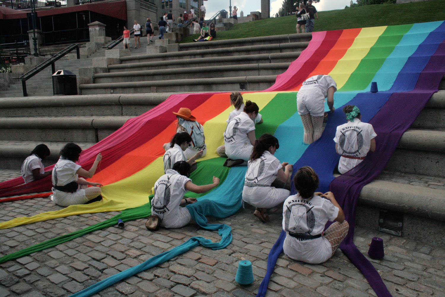 multiple people knitting a rainbow colored textile