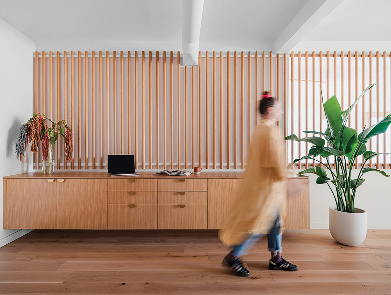 A woman walking in a room with a wooden wall.