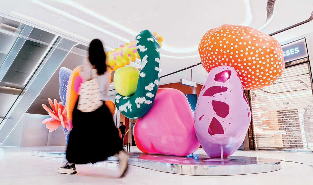 A woman walking past a large sculpture of colorful balloons.