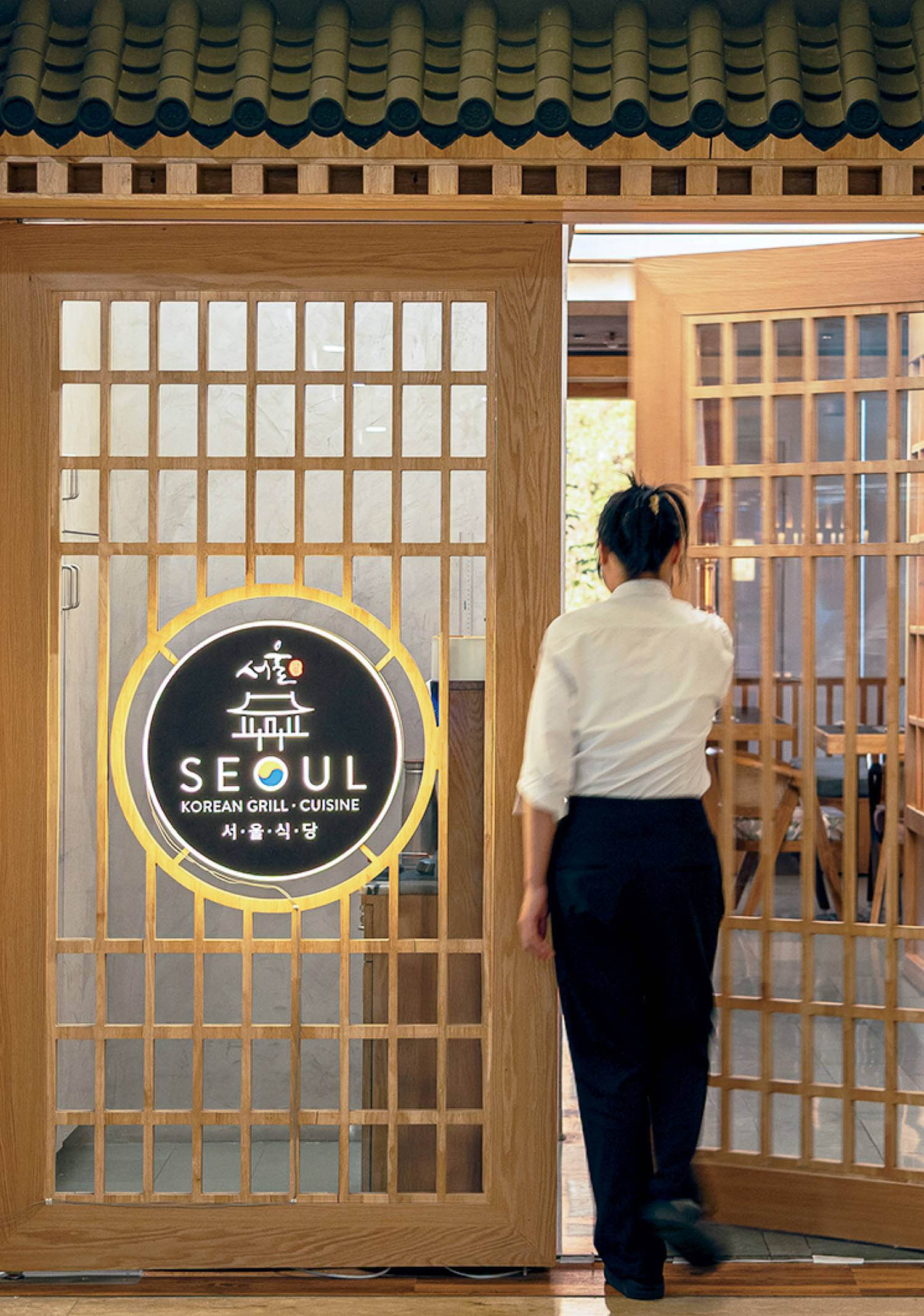 A woman is entering a restaurant through a glass door.