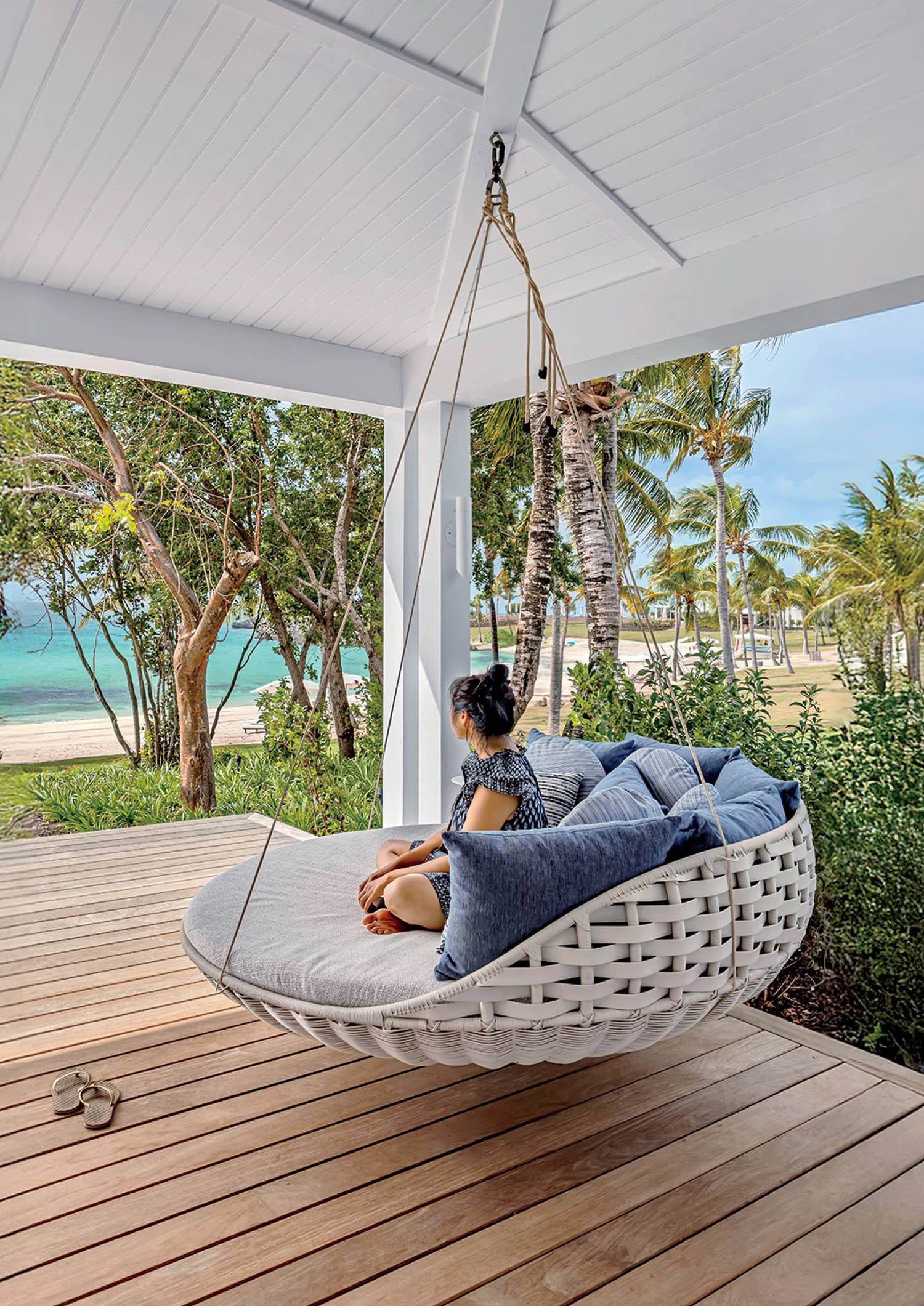 A woman sitting in a white hanging chair on a porch.