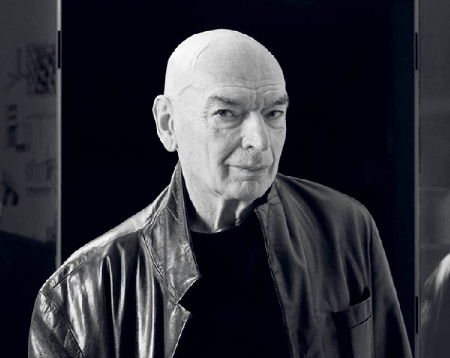 A man in a leather jacket standing in front of a mirror.