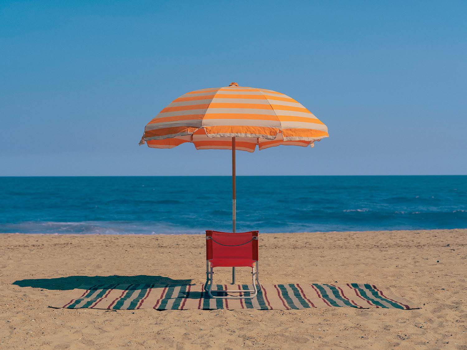 A beach chair and umbrella on a beach.