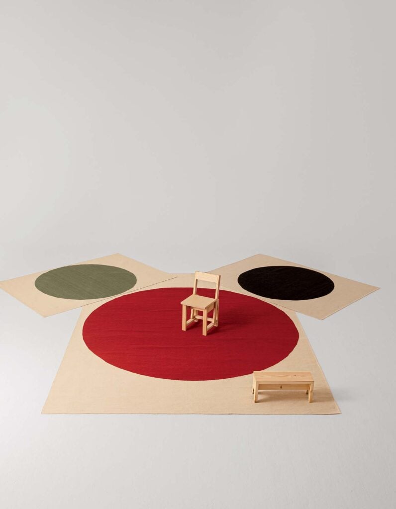 A wooden chair and a red rug on a white surface.