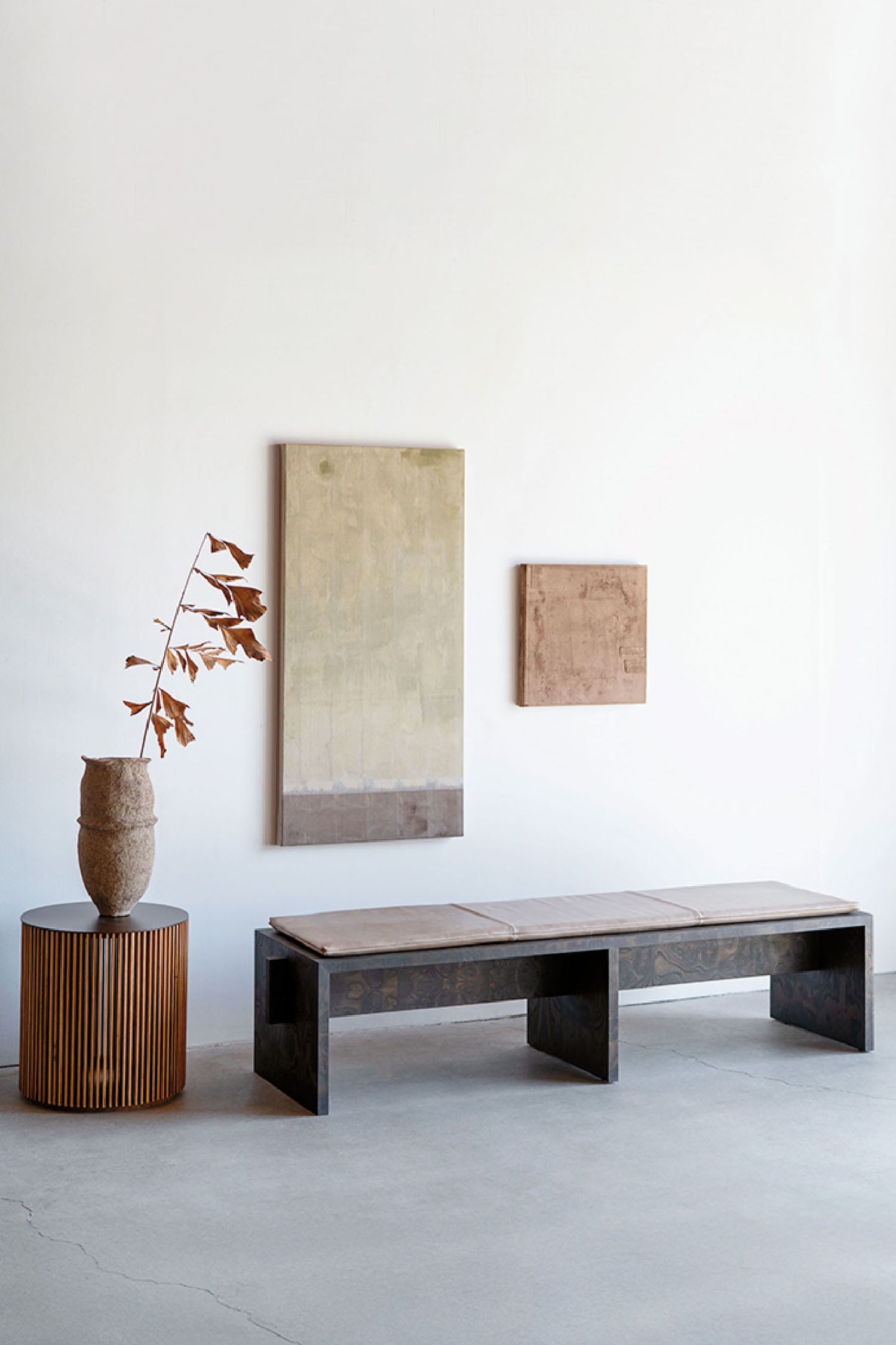 A wooden bench and a vase on a concrete floor.