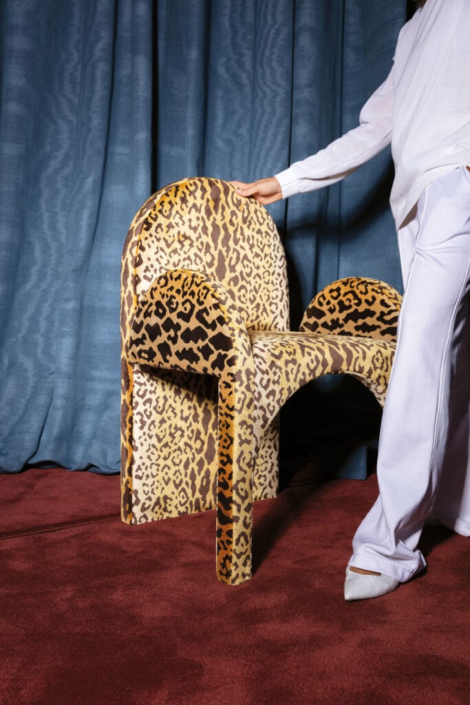 A man in a white shirt is standing next to a leopard chair.
