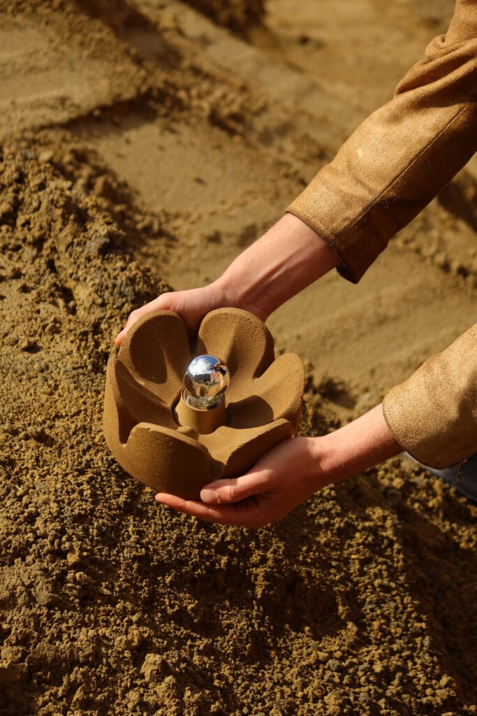 hands holding a tan flower shaped lamp above sand