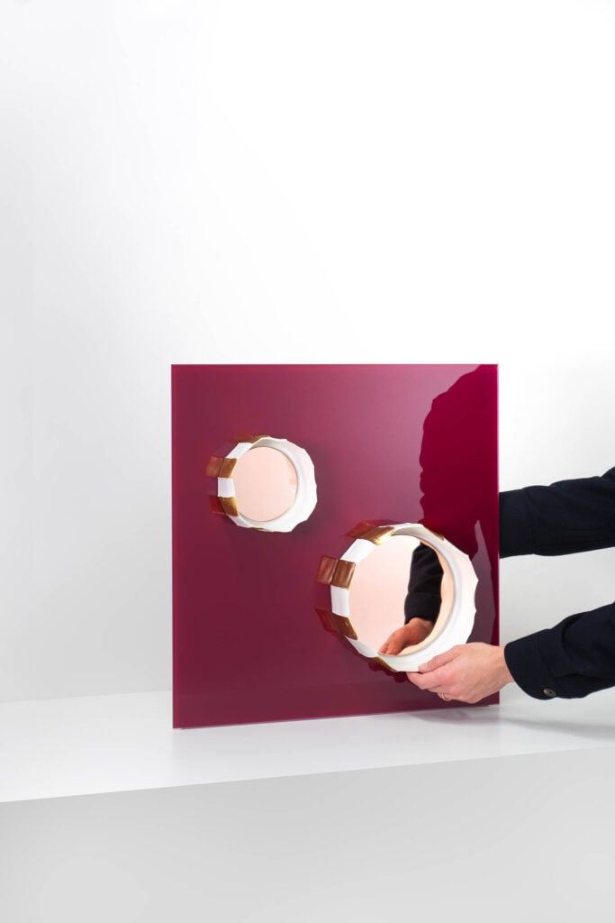 hands reaching for a burgundy square with circle shaped mirrors