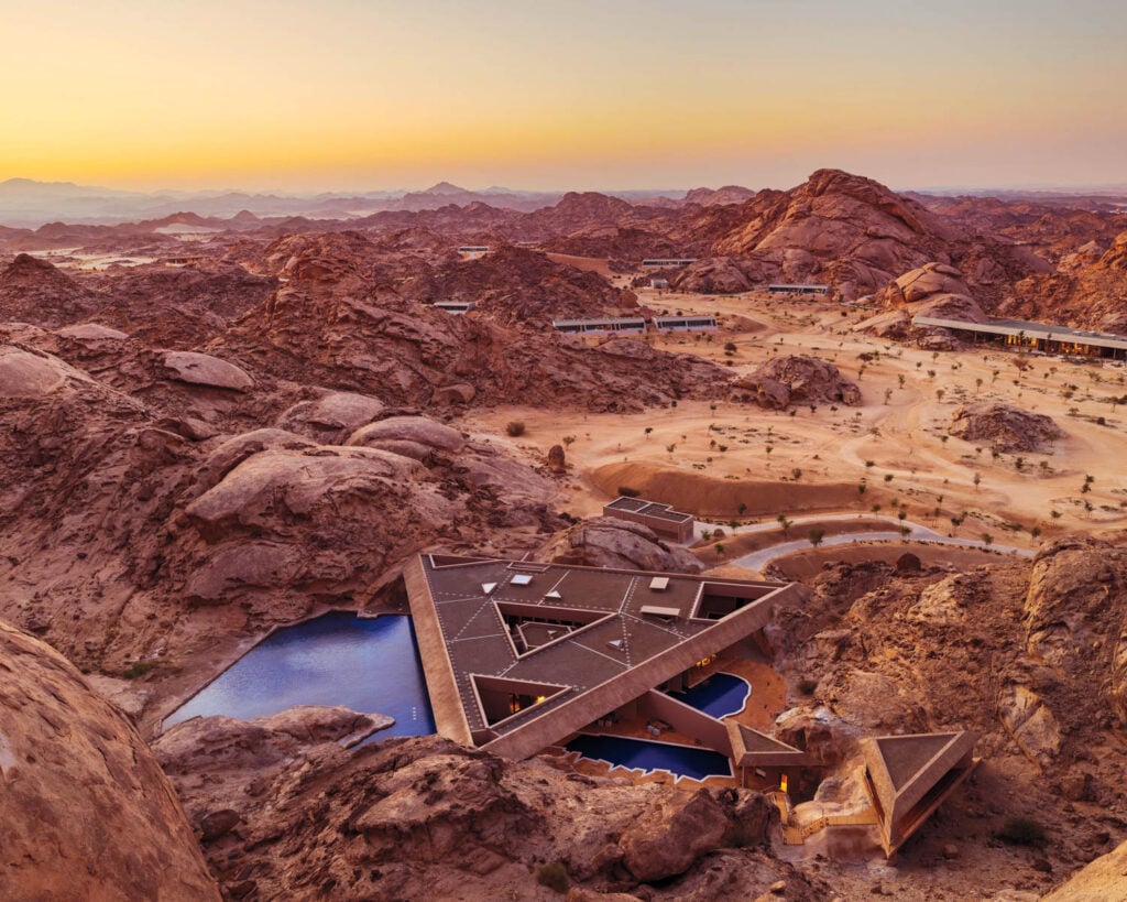 Modern triangular building nestled in rocky, desert landscape at sunset
