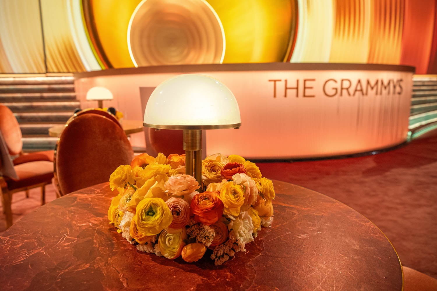 जीवंत पीले और नारंगी फूलों से घिरे हुए हल्के रोशनी वाले टेबल लैंप के साथ एक गर्म, सुरुचिपूर्ण सेटिंग।