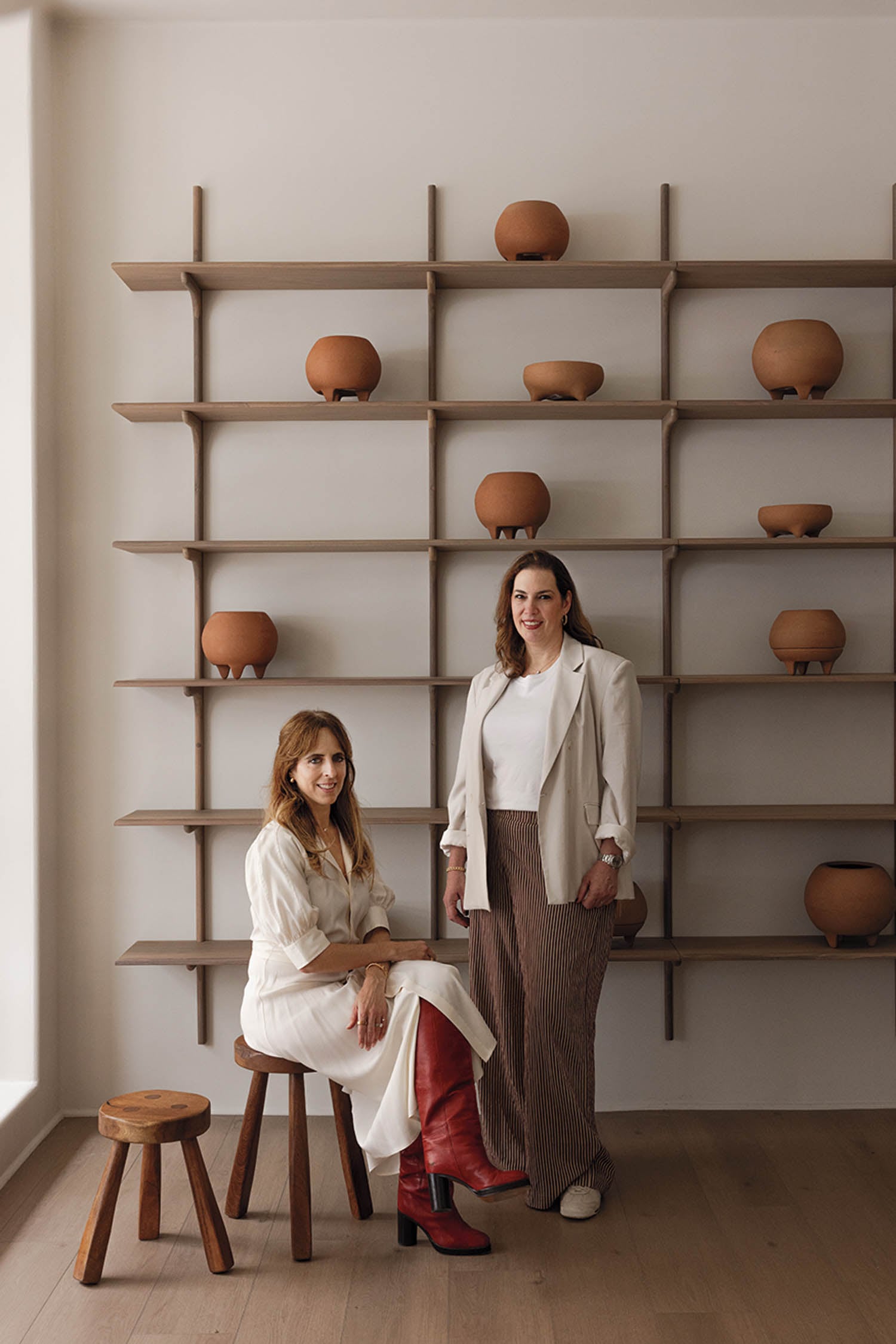 Two women sitting on a wooden bench in front of a wall of shelves