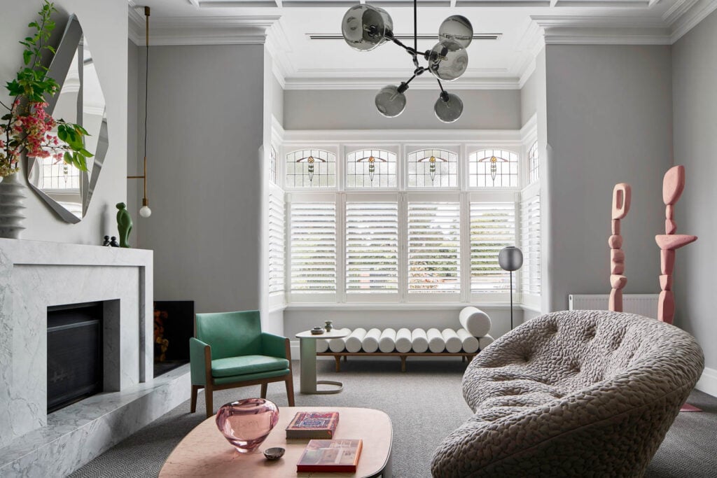 Stylish living room with a modern chandelier, marble fireplace, and large window with shutters