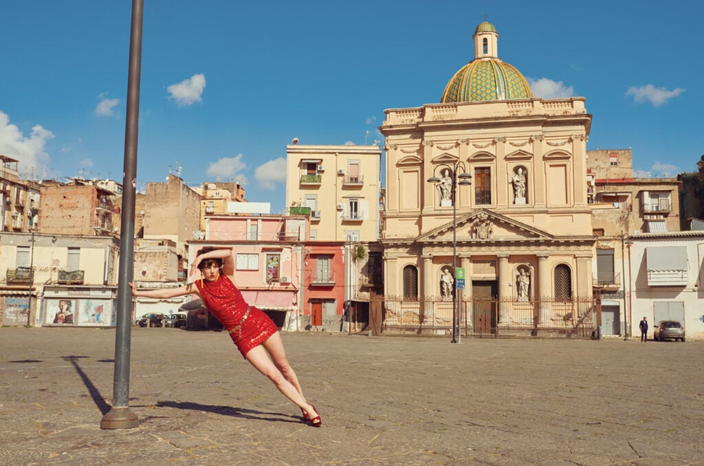 A woman in a red dress is leaning on a street sign.