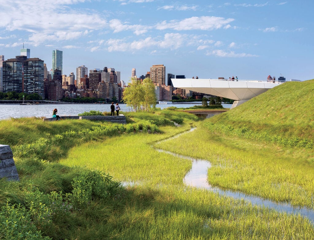 A grassy field with a river and buildings in the background.