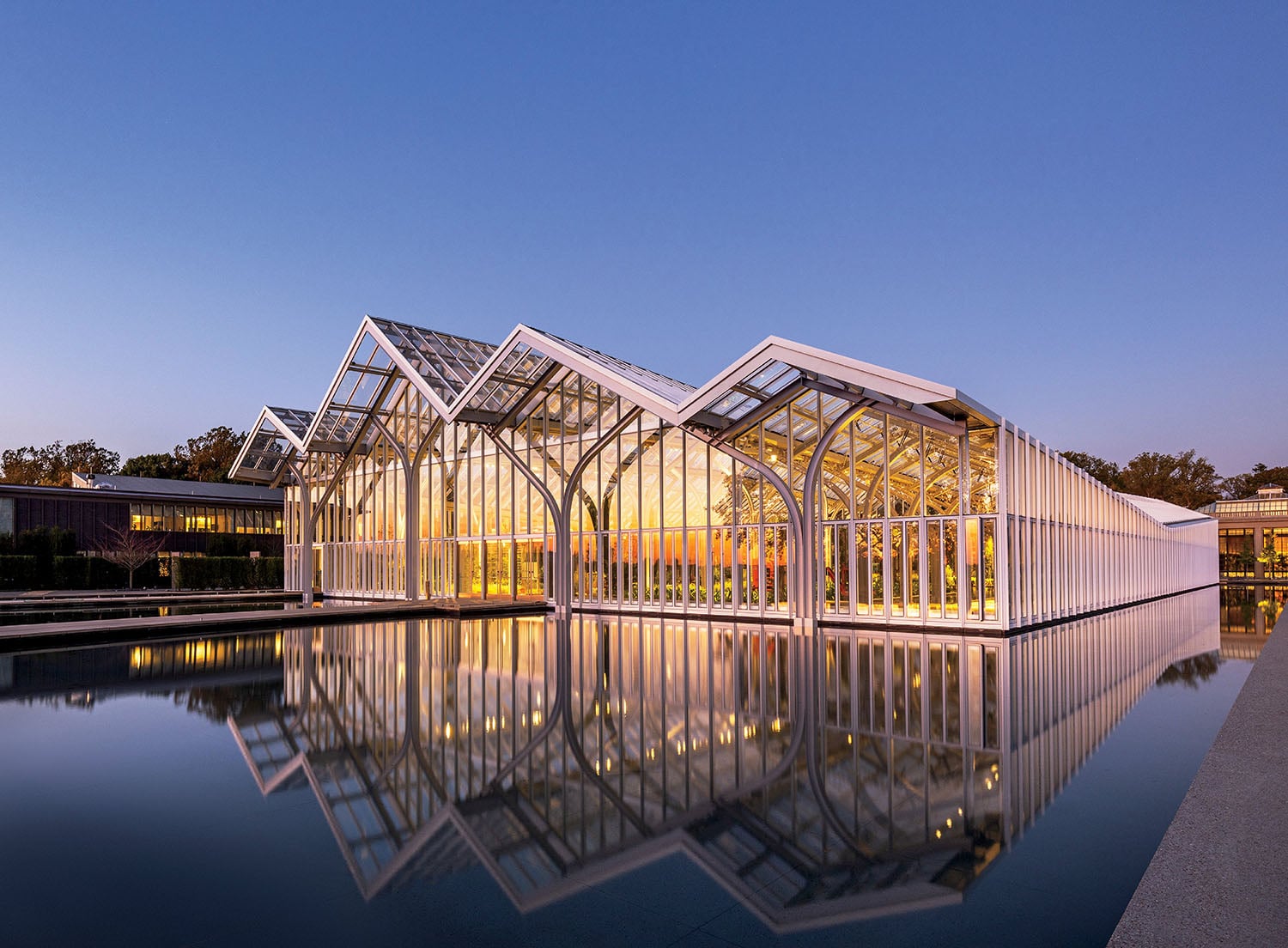 A glass house with a pool in the fore.