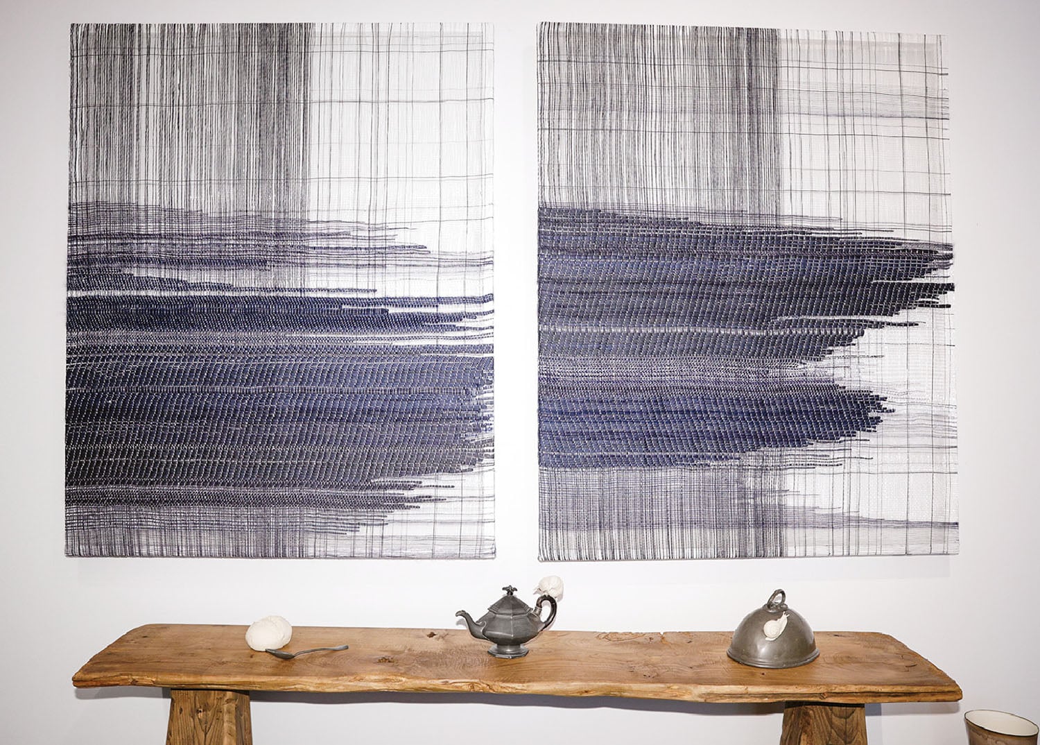 Two paintings on a wall with a wooden table.