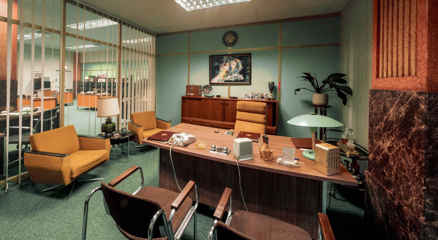 A retro 1970s office with wood furniture, green carpet, and pastel walls