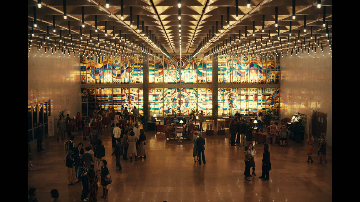 A spacious, brightly lit lobby features a vibrant, multicolored stained glass wall