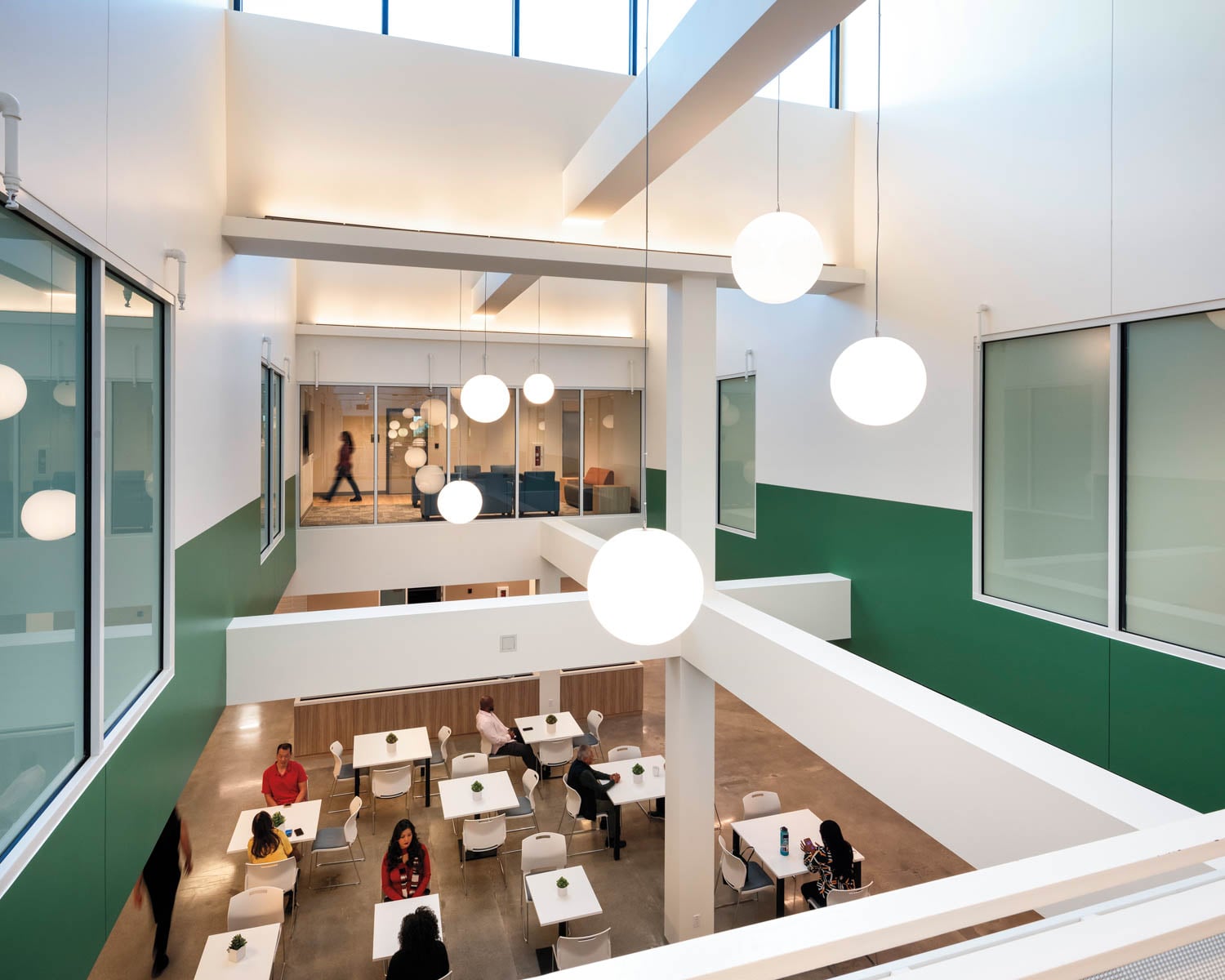 Modern atrium with green and white walls, large hanging globe lights, and a mezzanine
