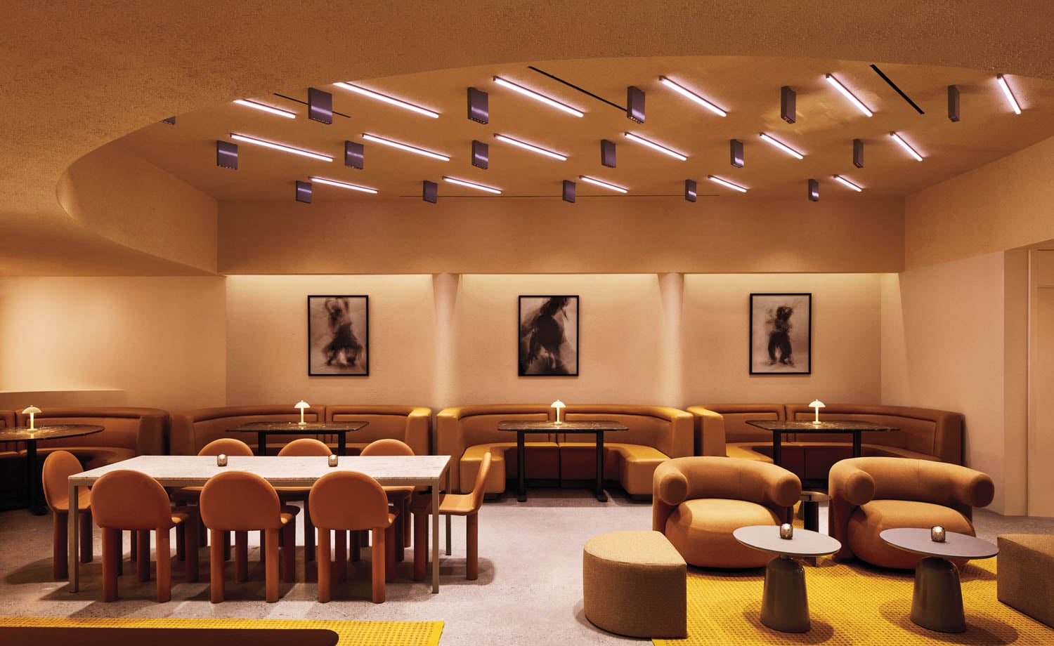 Modern, warmly lit lounge with curved seating, abstract art on light beige walls, and unique ceiling lights