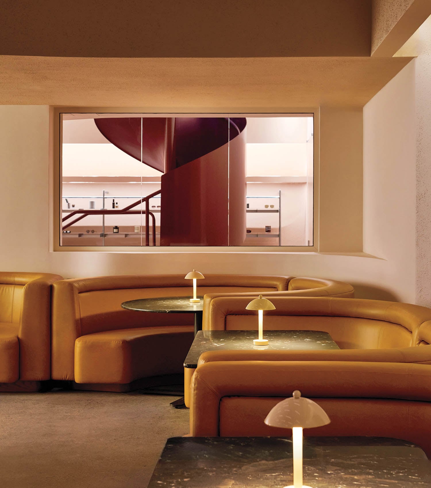 A cozy lounge with curved orange booths and small round tables featuring warm-lit lamps