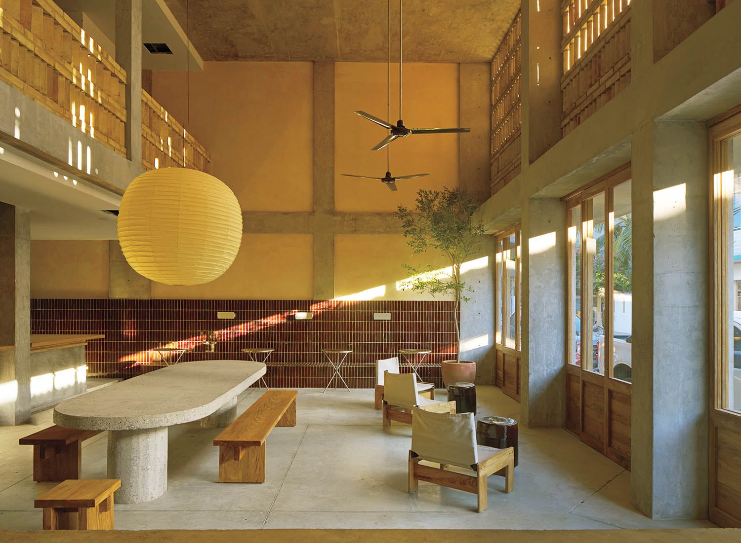 Spacious, warmly-lit room with high ceilings, large paper lantern, wooden furniture, potted plant, and modern accents