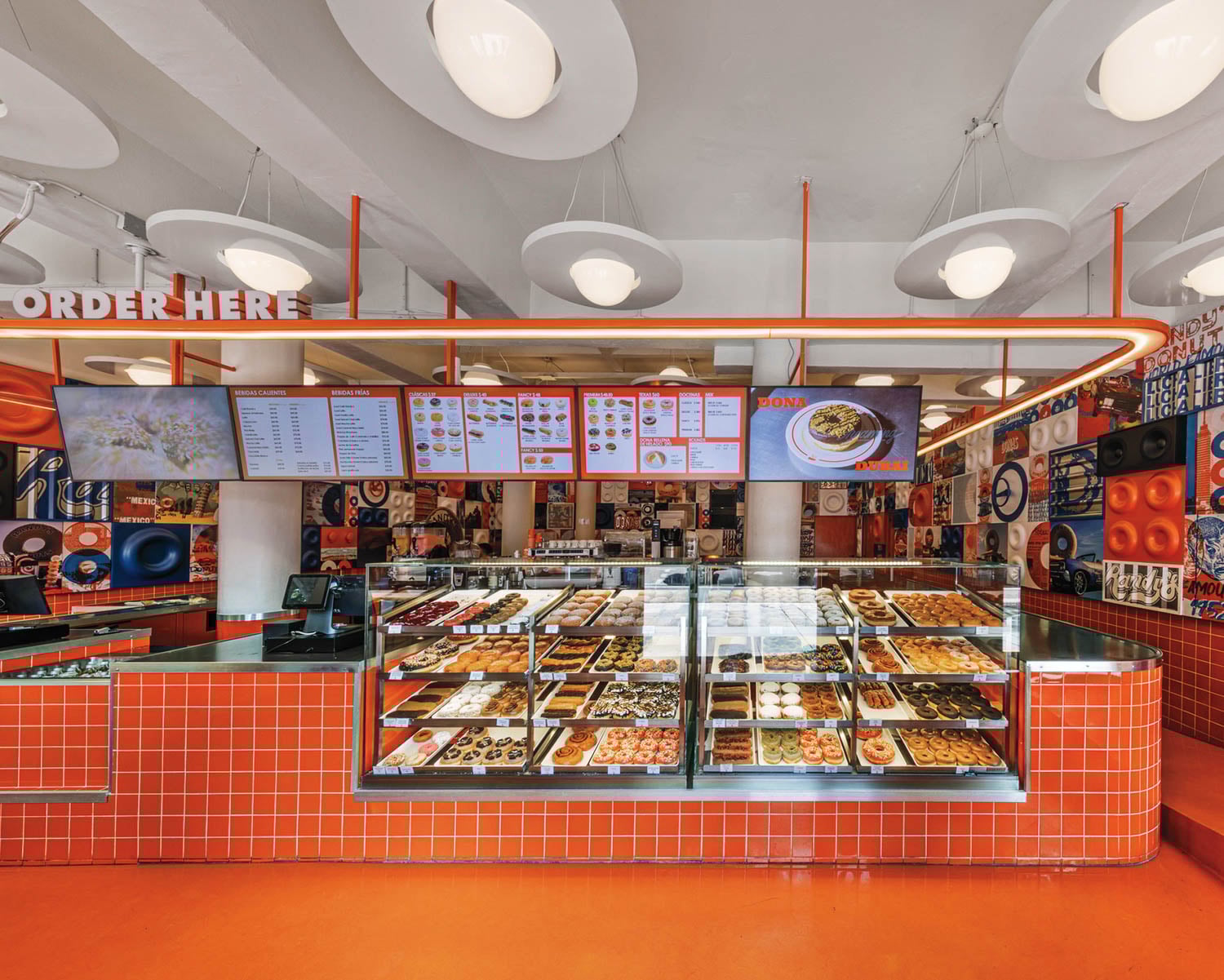 Bright donut shop with orange tiles, a glowing "Order Here" sign, glass display of assorted donuts
