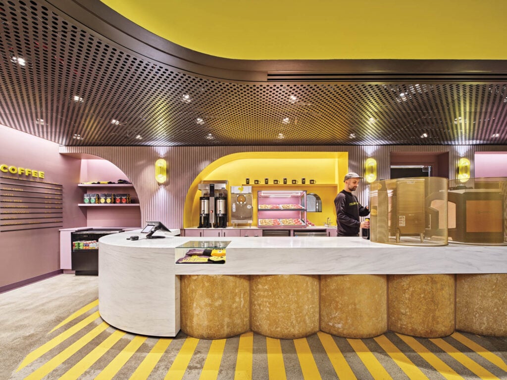 Modern cafe interior with bright yellow and purple decor, featuring a curved counter with baked goods