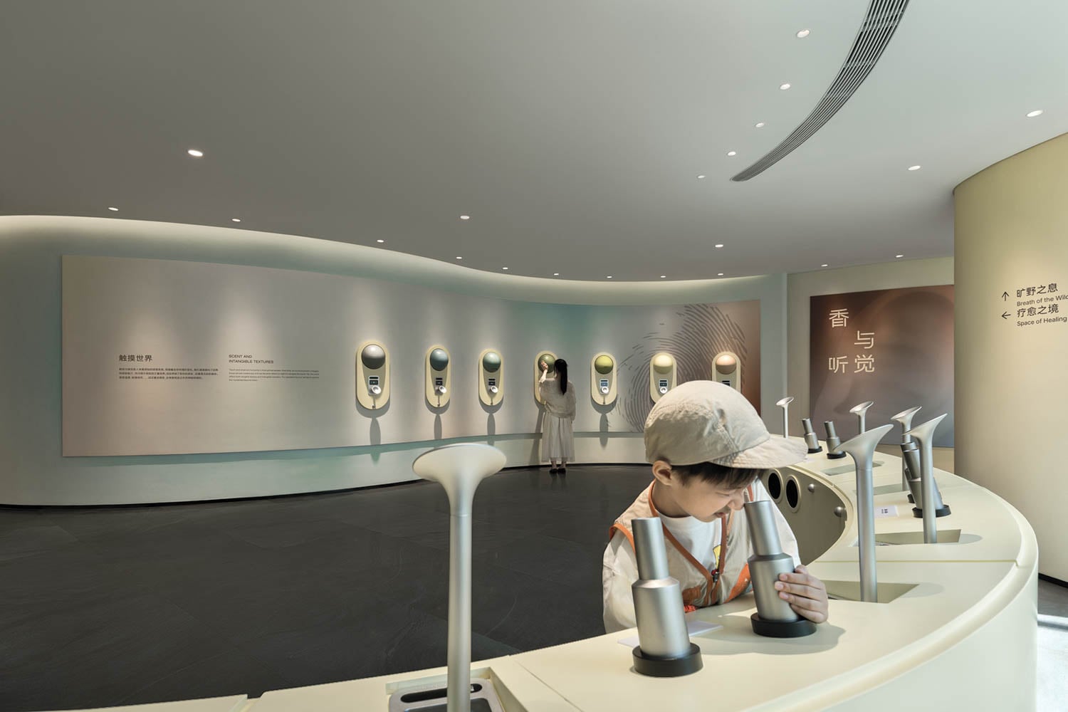 A child in a cap explores a sensory exhibit by smelling through funnels